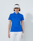 Woman wearing a blue polo shirt, white pants, and a visor on a light gray background