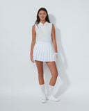 Person wearing a white sleeveless top and pleated skirt with white shoes on a plain background