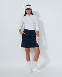 Woman in golf attire including a white shirt, navy skirt, and white shoes on a light gray background