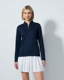 Woman wearing a navy long-sleeve top and white pleated skirt on a light gray background