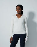 Woman wearing a white sweater and dark pants against a light gray background