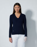 Woman wearing a navy sweater and white pants against a gray background