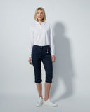 Woman wearing a white shirt and dark navy capris against a plain background