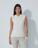 Woman wearing a white sleeveless knitted top and light gray pants against a plain background