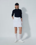 Person wearing a navy shirt, white skirt, and white shoes on a plain background
