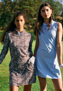 Two girls standing on a golf course wearing brown and light blue.