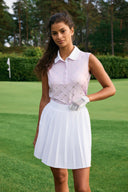Girl wearing a pink sleeveless top and white pleated skort standing on a golf course.