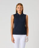A woman modeling a sleeveless navy polo shirt with a half-zip collar, paired with white pants and a white glove, against a light gray studio background.