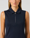 A woman wearing a sleeveless dark navy polo-style top with a short front zipper, shown from the shoulders to the waist against a light gray studio background.