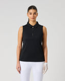 A woman modeling a sleeveless black polo shirt with a half-zip collar, paired with white pants, against a solid light gray background.