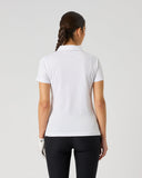 A woman viewed from the back wearing a white short-sleeve polo shirt and black pants against a plain light gray studio background.