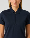 A woman wearing a dark navy blue short-sleeve polo shirt with a half-zip collar, shown from the chest up against a light gray studio background.