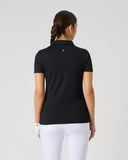 A woman viewed from the back wearing a black short-sleeve polo shirt and white pants against a light gray studio background.