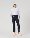 A woman modeling a white long-sleeve polo shirt, navy blue cropped golf pants, a white visor, white gloves, and white golf shoes against a light gray studio background.