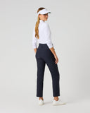 A woman modeling a pair of dark navy blue golf pants, paired with a white long-sleeve shirt, white visor, and white sneakers, shown from a side-back angle against a light gray studio background.