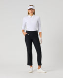 A woman modeling a white long-sleeve polo shirt, black cropped golf pants, a white visor, white golf gloves, and white golf shoes against a light gray studio background.