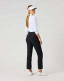 A woman modeling black golf pants, a white long-sleeve top, a white visor, and white golf shoes, shown from a side-back angle against a light gray studio background.