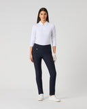 A woman modeling a white long-sleeve polo shirt and navy blue fitted pants, standing against a light gray studio background.
