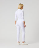 A woman with blonde hair is shown from behind wearing a white long-sleeve mock neck top and matching white leggings, paired with white sneakers, against a light gray studio background.