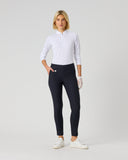 A woman modeling a white long-sleeve polo shirt and dark navy athletic leggings with white sneakers, standing against a light gray studio background.