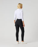 A woman with blonde hair is shown from behind wearing black skinny pants, a white long-sleeve top, and white sneakers against a light gray studio background.