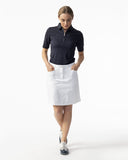 Woman wearing a navy polo shirt and white skirt on a white background
