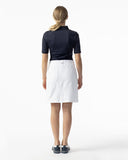 Woman wearing a navy polo shirt and white skirt on a white background
