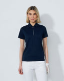 Woman wearing a navy blue polo shirt and white pants on a light gray background