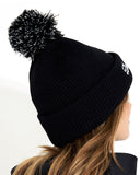 Black beanie with pom-pom worn by a person on a white background
