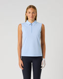 A woman modeling a light blue sleeveless polo shirt with a half-zip collar, paired with dark pants and a white golf glove, against a light gray studio background.