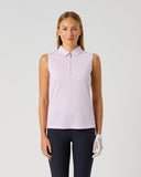 A woman modeling a sleeveless light pink polo shirt with a half-zip collar, paired with dark navy pants and a white golf glove, against a plain light gray studio background.