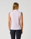 A woman viewed from the back wearing a sleeveless light pink polo shirt and dark navy pants, standing against a plain light gray studio background.
