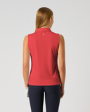 A woman viewed from behind wearing a sleeveless collared red top and dark navy leggings against a light gray studio background.