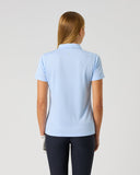 A woman viewed from behind wearing a light blue short-sleeve polo shirt and dark navy pants, standing against a plain light gray studio background.