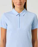 A woman wearing a light blue short-sleeve polo shirt with a half-zip collar, shown from the chest up against a plain light gray studio background.
