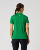 A woman viewed from behind wearing a bright green short-sleeve polo shirt and black leggings against a light gray studio background.
