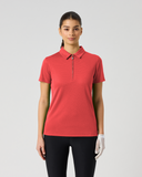 A woman modeling a short-sleeve polo shirt in a solid coral red color, featuring a half-zip collar, paired with black pants and a white glove, set against a plain light gray background.