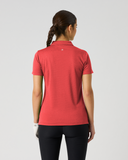 A woman viewed from the back wearing a short-sleeve collared polo shirt in a muted coral red color, paired with black leggings, against a plain light gray studio background.
