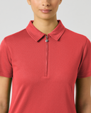 A woman wearing a coral red short-sleeve polo shirt with a half-zip collar, shown from the nose down against a light gray studio background.