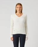A woman modeling a ribbed knit V-neck sweater in off-white, paired with dark navy leggings, against a plain light gray studio background.