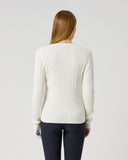 A woman viewed from behind wearing a cream-colored, long-sleeve cable-knit sweater and dark navy leggings against a light gray studio background.