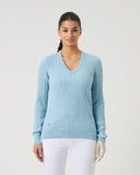 Woman wearing a light blue sweater and white pants on a plain background