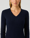 A woman wearing a dark navy blue ribbed V-neck sweater, shown from the nose down against a light gray studio background.