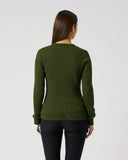 A woman viewed from the back wearing an olive green ribbed knit sweater and black pants, standing against a plain light gray studio background.
