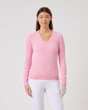 Woman wearing a pink ribbed sweater and white pants on a light gray background