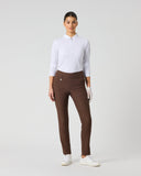 A woman modeling slim-fit brown trousers, paired with a white long-sleeve polo shirt and white golf shoes, standing against a light gray studio background.