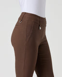 A close-up side view of a person wearing brown riding breeches with a white top, shown against a plain light gray studio background.