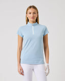 Woman wearing a light blue equestrian shirt and white pants on a plain background