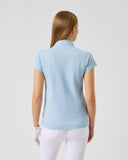 Woman wearing a light blue polo shirt and white pants on a plain background