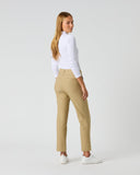 A woman wearing beige straight-leg trousers, a white long-sleeve top, and white sneakers, photographed from the back against a light gray studio background.